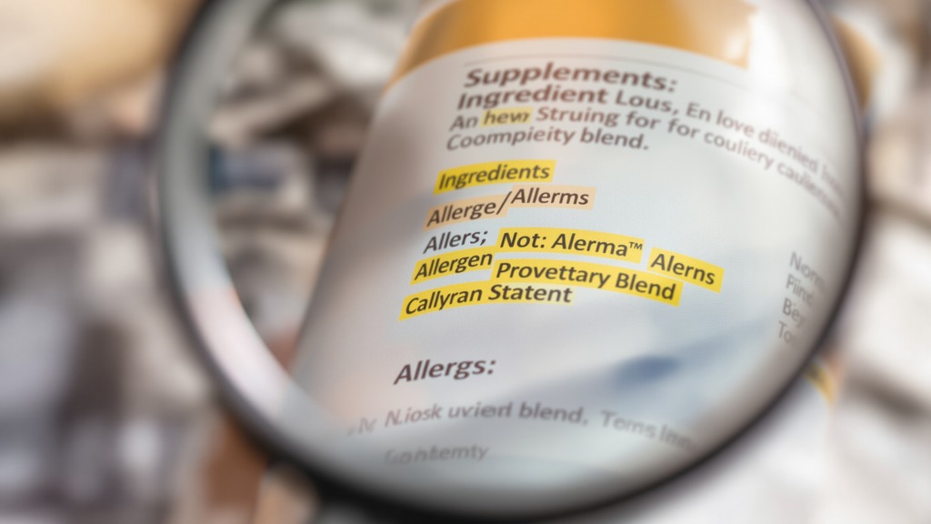 Magnifying glass over an unbranded supplement label showing ingredient forms, allergens, and a proprietary blend.